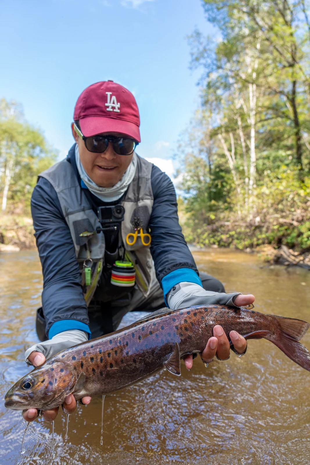 Zeo holding a catch in a wooded stream
